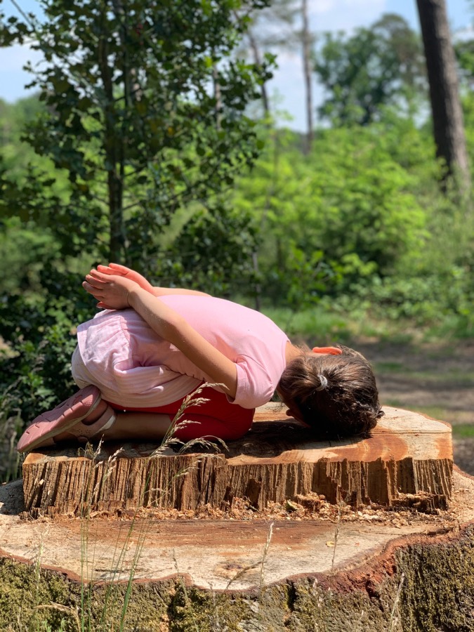 Kind in Yogahaltung auf einem Baumstamm